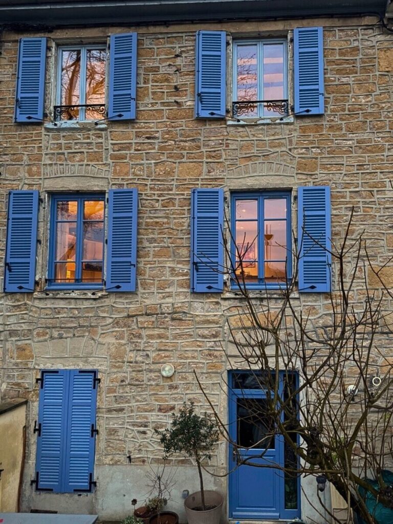 Façade maison en pierre rénovée avec volets battants bois persiennés finition bleu pigeon