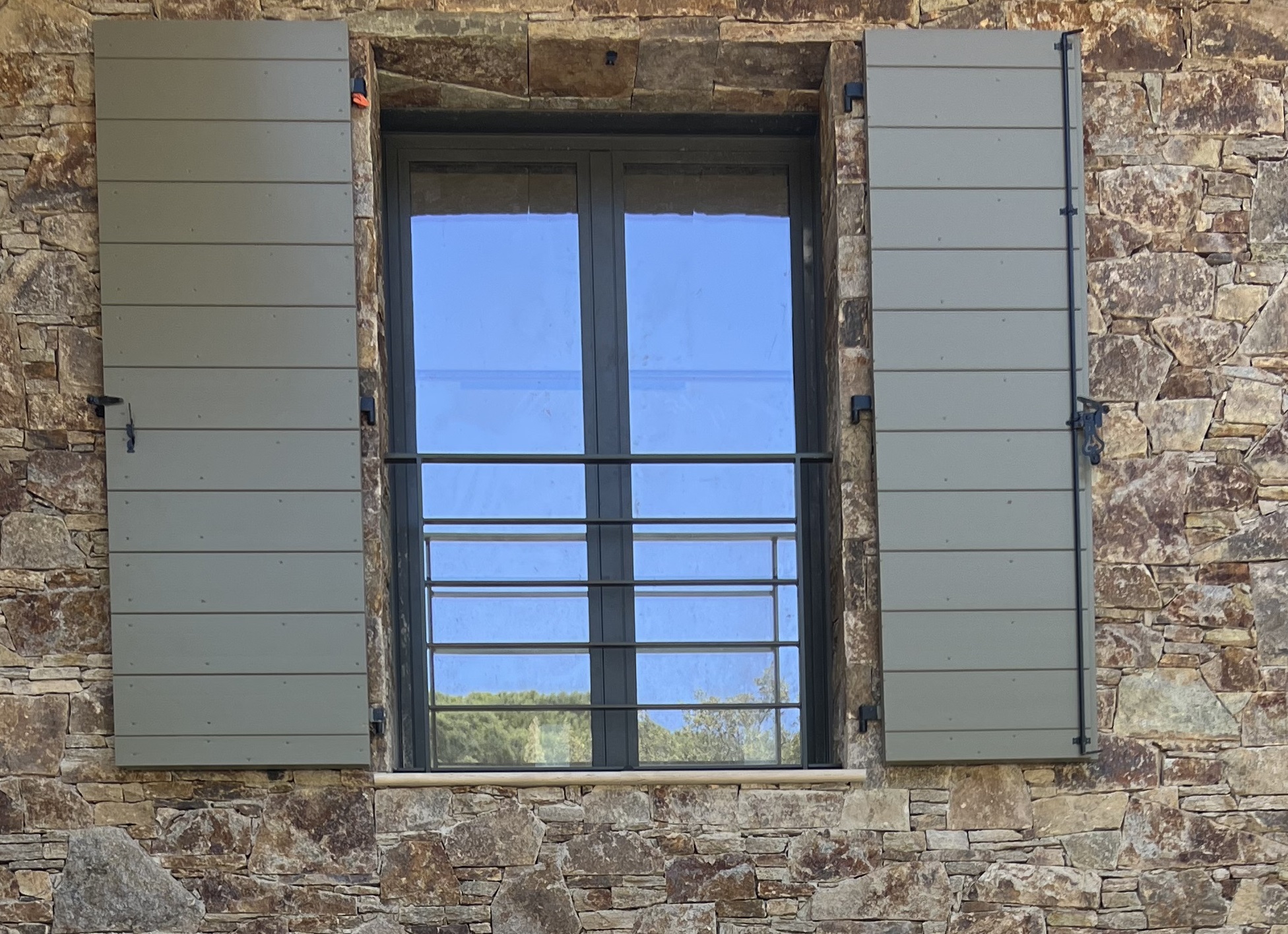 Vue intérieure volet Provençal bois massif 47 mm fermé, baie vitrée façade Sud